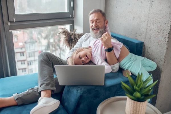 Ein reifer Mann mit Laptop sitzt neben seiner kleinen süßen Tochter — Stockfoto