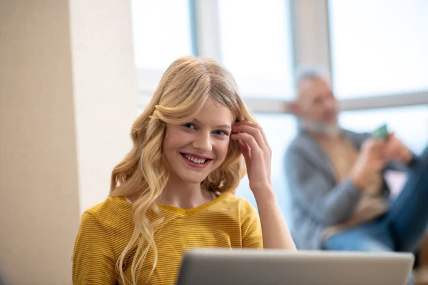 Uma linda garota loira sentada no laptop e sorrindo — Fotografia de Stock