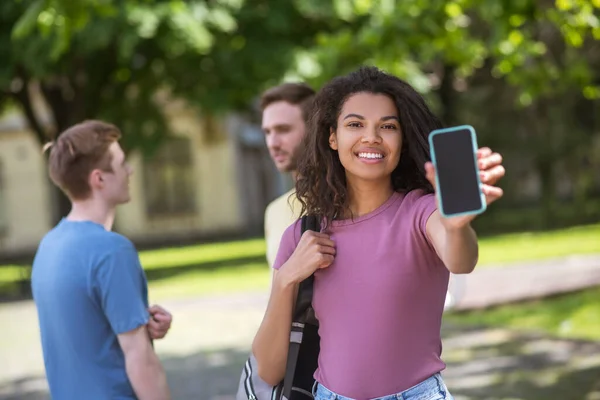 Tre unga människor med smartphones i händerna tillbringar tid i parken — Stockfoto