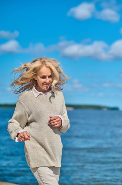 Gülümseyen orta yaşlı kadın denizin kenarında koşuyor.