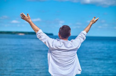 Elleri havada ve kameraya dönük bir adam.