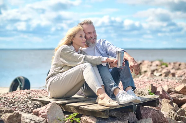 Щасливий чоловік і жінка з термосом, що сидить біля моря — стокове фото