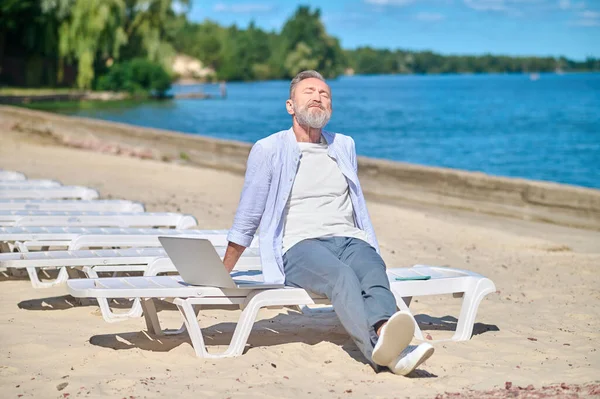 Άνθρωπος ηλιοθεραπεία συνεδρίαση με φορητό υπολογιστή στην παραλία — Φωτογραφία Αρχείου
