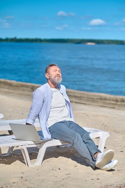 Hombre relajante cerca del ordenador portátil en la tumbona de playa — Foto de Stock