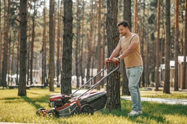 Çim biçme makinesiyle çimenlerde yürüyen adam