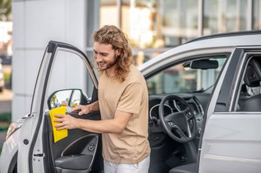 Neşeli genç adam arabanın kapısını temizliyor.