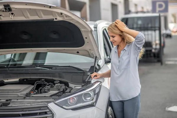 Upset woman looking into open hood of car — Stock Photo, Image