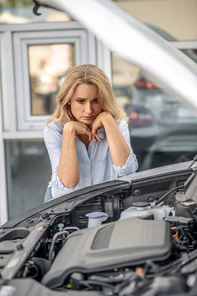 Pensive woman looking sadly into open hood of car — Stock Photo, Image