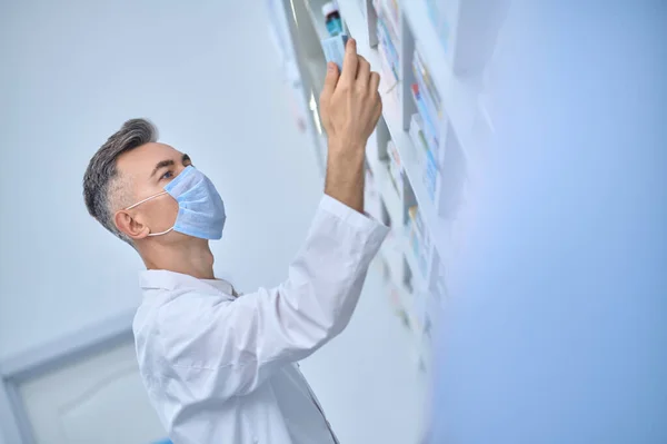 Pharmacist in protective mask considering medication with interest — Stock Photo, Image