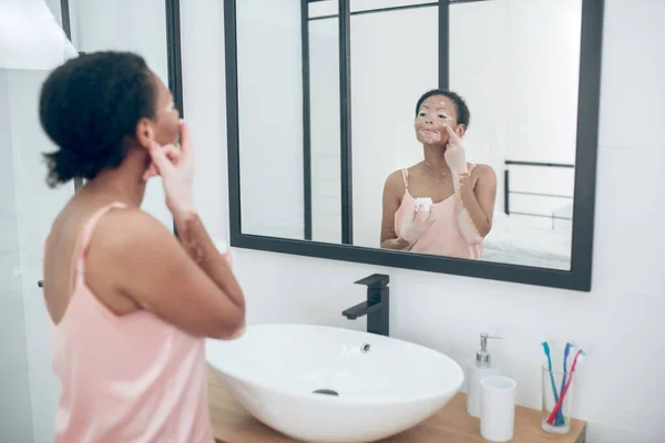 Una linda joven aplicando crema hidratante en su cara — Foto de Stock