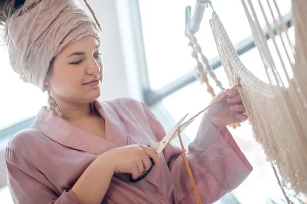 Молодая женщина в домашнем платье обрезает пряжу — стоковое фото