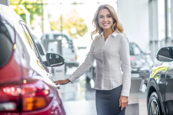 Smiling woman touching car door in dealership — Stock Photo, Image