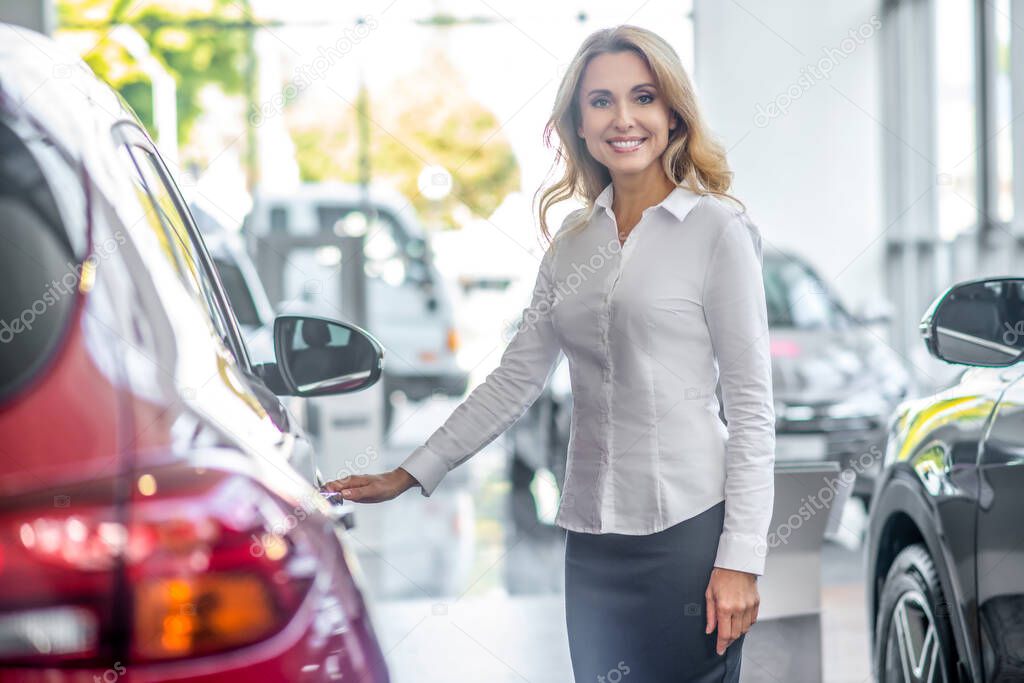 Smiling woman touching car door in dealership