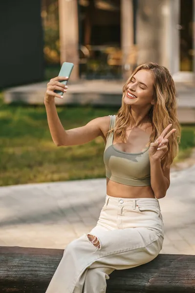 Glada kvinna med smartphone visar frihet tecken med fingrar — Stockfoto