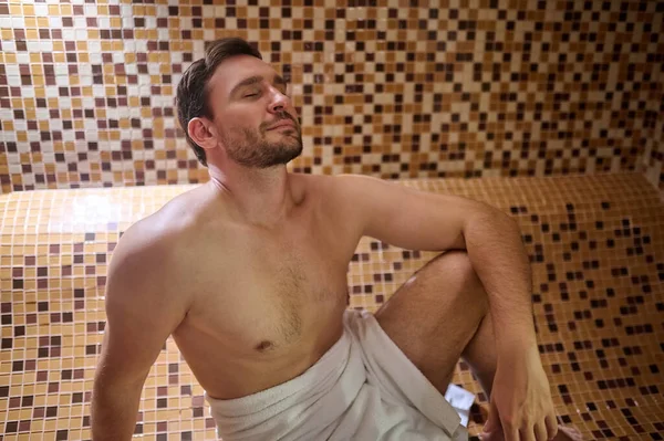 Havlu giymiş bir adam saunada oturuyor ve detoks seansı yapıyor. — Stok fotoğraf