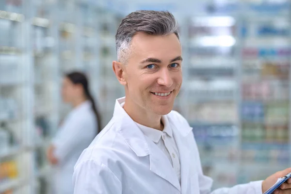 Веселый мужчина в белом халате в аптеке — стоковое фото