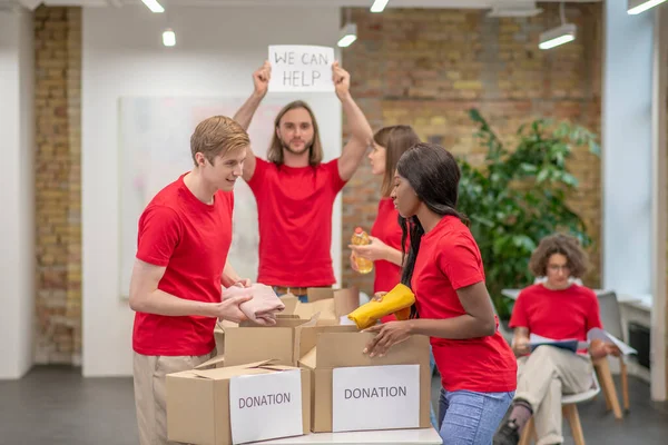 Jovens voluntários em camisetas vermelhas distribuindo doações em um centro de triagem — Fotografia de Stock
