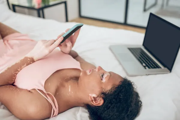 Seorang wanita berbaring di tempat tidur dan memegang gadget di tangannya — Stok Foto