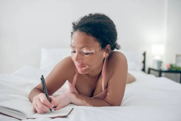 Eine junge Frau schreibt in ihr Tagebuch und sieht inspiriert aus — Stockfoto
