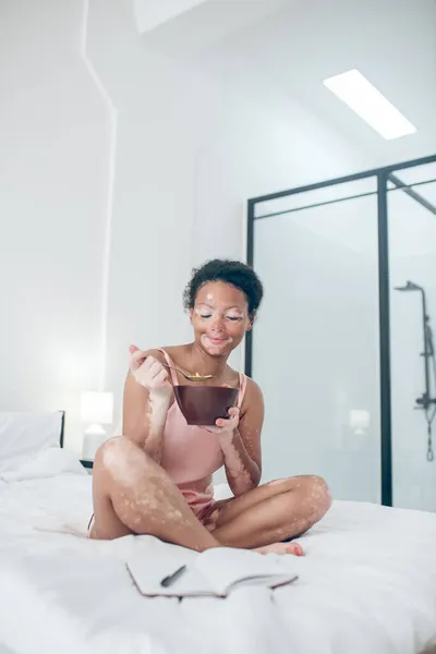Una donna seduta sul letto e che fa colazione — Foto Stock