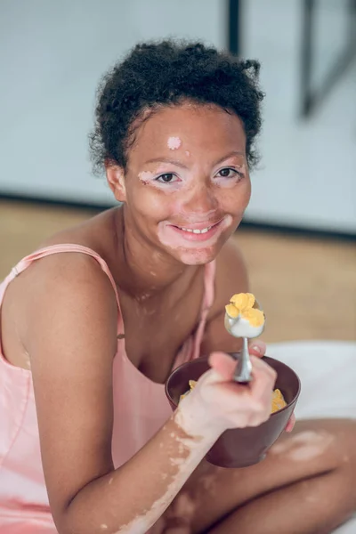 Una mujer de piel oscura comiendo cereales mientras está sentada en la cama — Foto de Stock