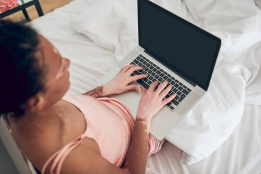 Yatakta oturmuş dizüstü bilgisayarla çalışan bir kadın.