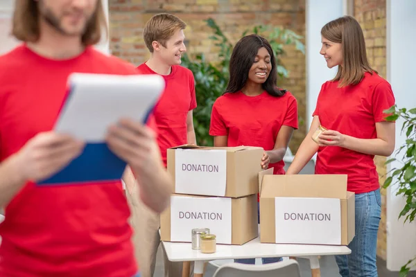 Fiatal önkéntesek piros pólóban a munkahelyükön egy elosztóhelyen — Stock Fotó