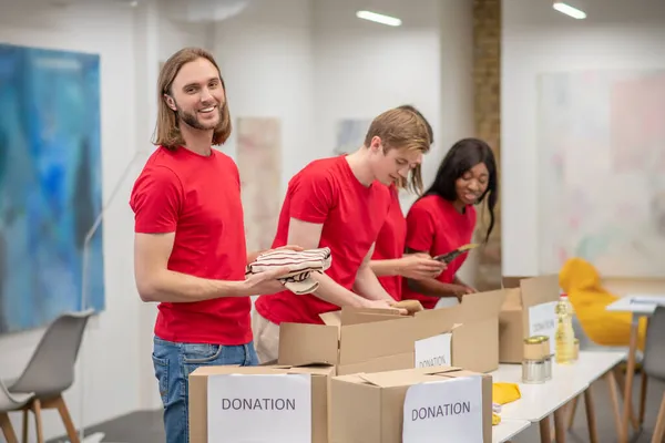 Unga människor i rött packar kartongerna med humanitär hjälp — Stockfoto