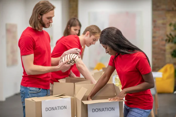 Mladí dobrovolníci v červených tričkách rozdělují dary v třídírně — Stock fotografie