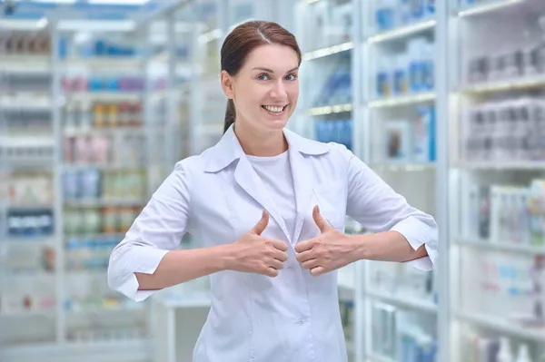 Веселая фармацевтка, стоящая в аптеке — стоковое фото
