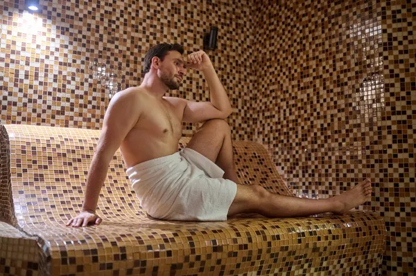 Havlu giymiş bir adam saunada oturuyor ve detoks seansı yapıyor. — Stok fotoğraf