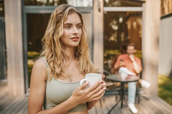 Pensive woman with cup and man behind near house — Stock Photo, Image