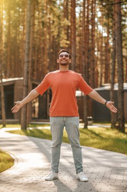 Parkta güneşin altında duran kendine güvenen gülümseyen adam.