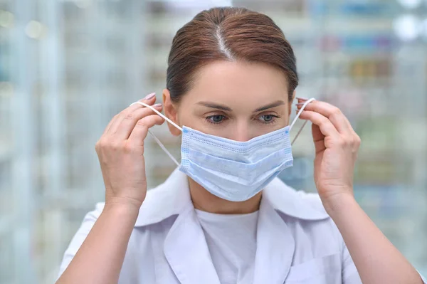 Mujer poniéndose máscara protectora en la farmacia —  Fotos de Stock