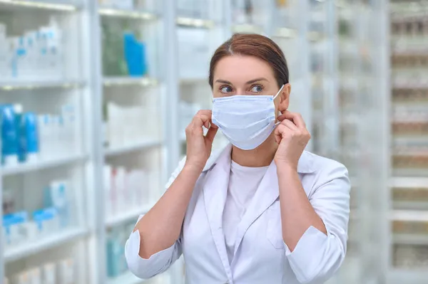 Zelfverzekerde vrouw in labjas en beschermend masker — Stockfoto