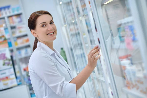 Mulher alegre farmacêutico abertura prateleira com medicamentos — Fotografia de Stock