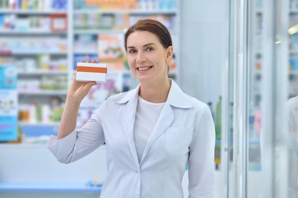 Mujer amigable con bata blanca mostrando medicina —  Fotos de Stock