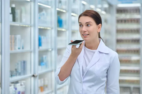 Ernsthafte Frau im weißen Kittel spricht Smartphone — Stockfoto