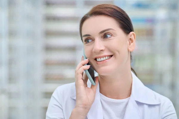 白いコートを着た笑顔の女性がスマートフォンで通信 — ストック写真
