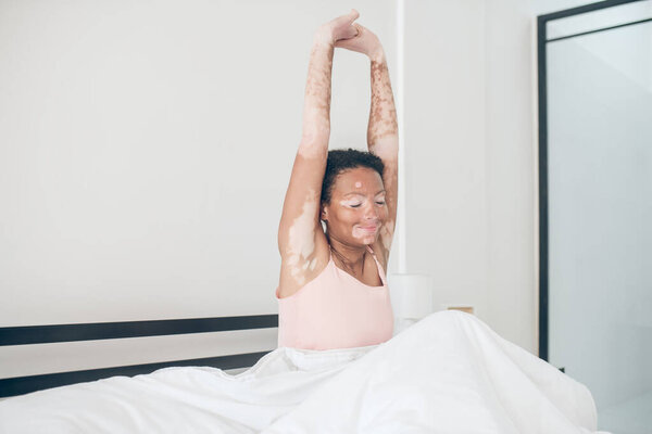 Милый молодой мулатка сидит в постели и выглядит расслабленным.
