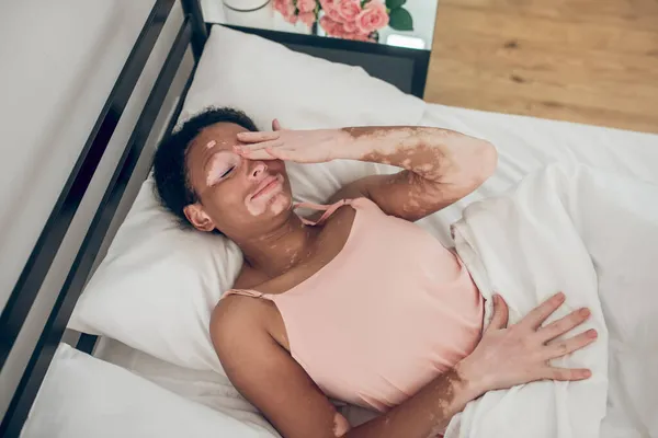 Een jonge donkere vrouw die in bed ligt, haar hand uitstrekt en glimlacht. — Stockfoto