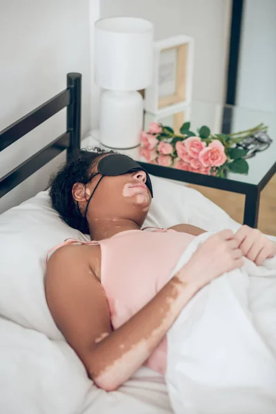 Μια νεαρή γυναίκα με μάσκα ύπνου ξαπλωμένη στο κρεβάτι. — Φωτογραφία Αρχείου