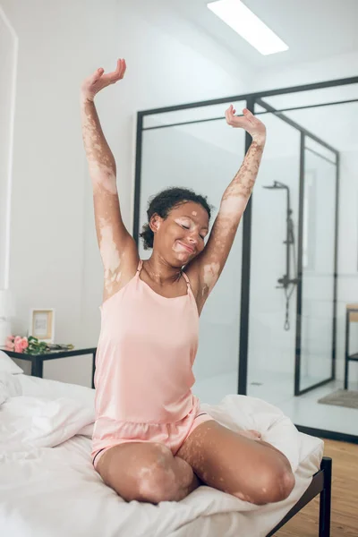 Seorang wanita muda yang lucu duduk di tempat tidur dalam lingerie merah muda dan peregangan — Stok Foto