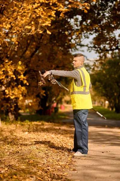 Een man in een geel vest met hark in het park — Stockfoto