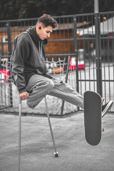 Guy appuyé sur des béquilles et touchant skateboard avec pied — Photo