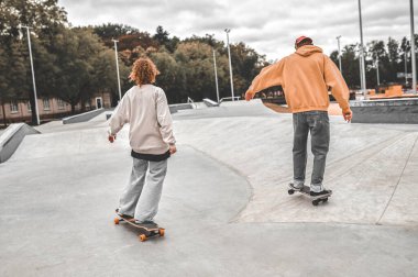 Kız ve erkek kameraya arkası dönük kaykay