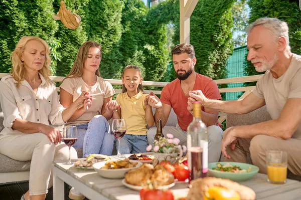 Eine Familie sitzt mit geschlossenen Augen und betet gemeinsam vor dem Abendessen — Stockfoto