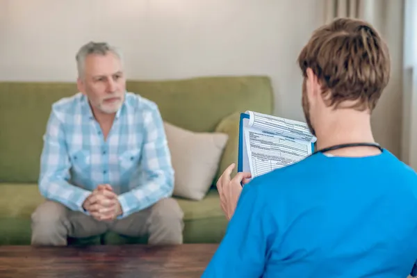 Hälso- och sjukvårdspersonal konsulterar en manlig patient i hemmet — Stockfoto