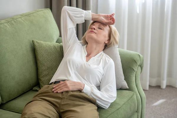 Mujer rubia de mediana edad tumbada en el sofá y sintiéndose mal — Foto de Stock