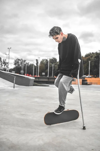 Guy ακουμπά σε πατερίτσες και αγγίζοντας skateboard με τα πόδια — Φωτογραφία Αρχείου